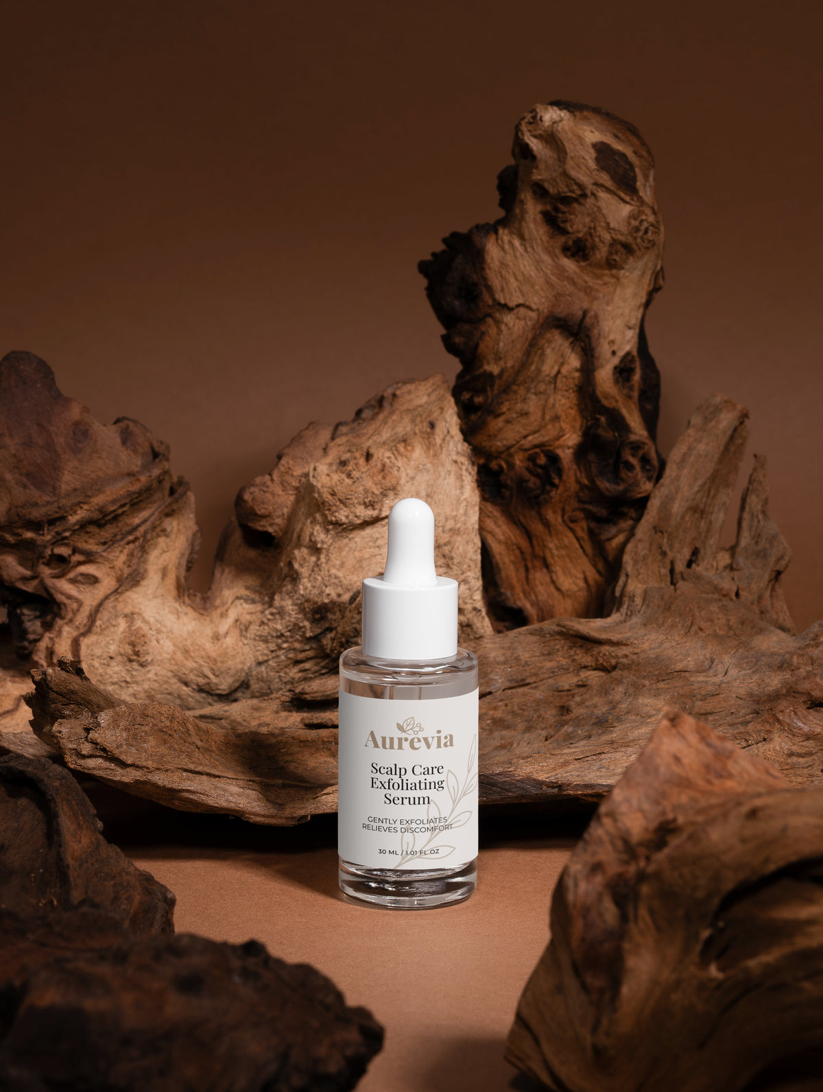 Aurevia Scalp Care Exfoliating Serum in clear bottle with dropper, set against rustic driftwood background