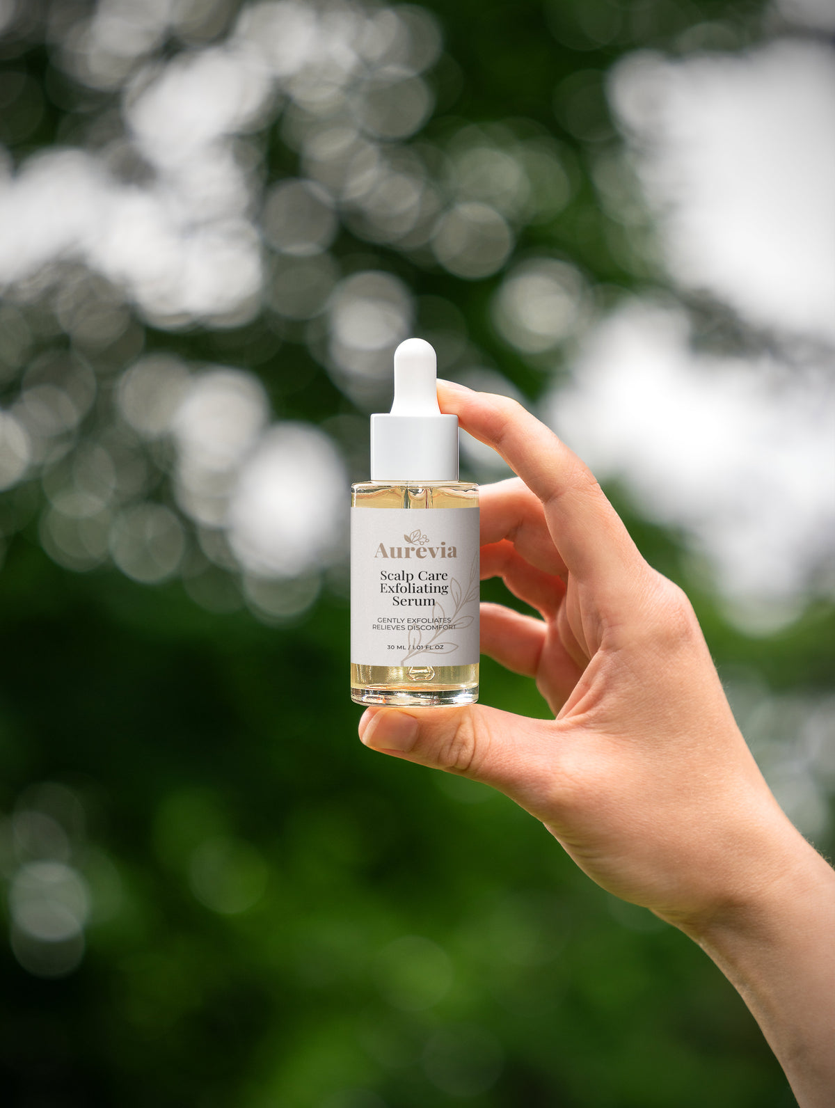 Aurevia Scalp Care Exfoliating Serum in hand against green bokeh background