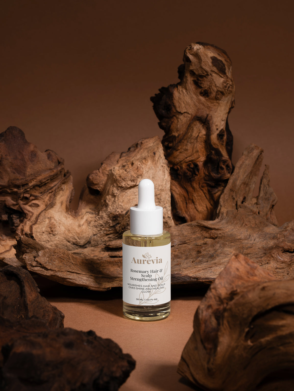 Rosemary Hair & Scalp Strengthening Oil in clear bottle with dropper, set against rustic driftwood background