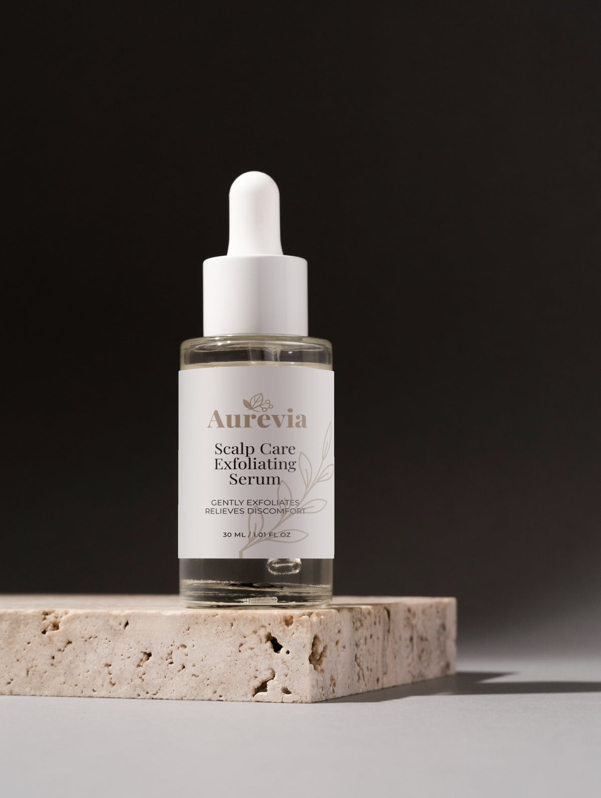 Aurevia Scalp Care Exfoliating Serum in clear glass bottle with dropper on stone base